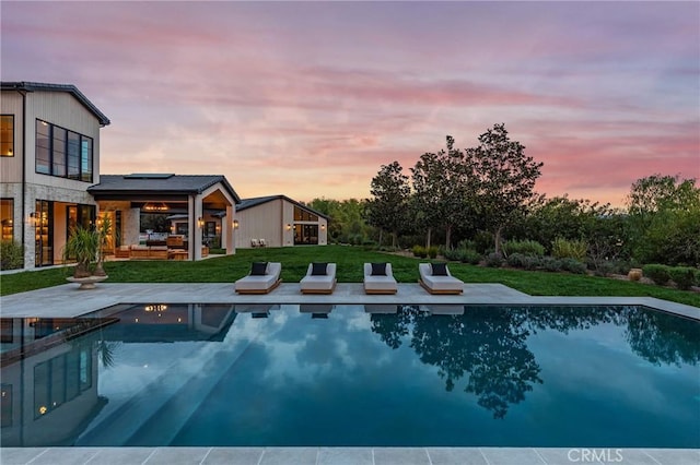 pool at dusk featuring a yard, a patio area, and an outdoor pool