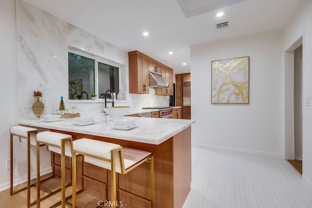 kitchen featuring recessed lighting, under cabinet range hood, visible vents, light countertops, and high end range