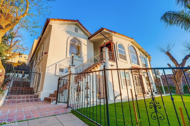 mediterranean / spanish house featuring stairway, a front yard, a tile roof, and stucco siding