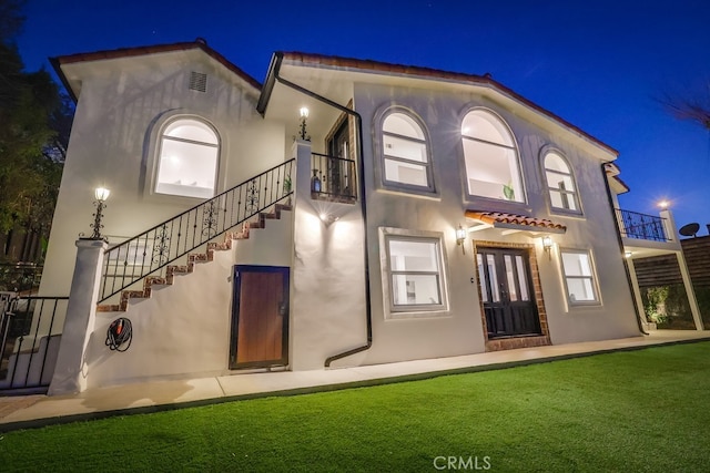 back of house at twilight featuring stairs, visible vents, and stucco siding