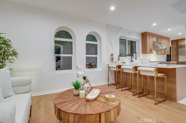 interior space with light wood-style floors, a breakfast bar, light countertops, under cabinet range hood, and recessed lighting