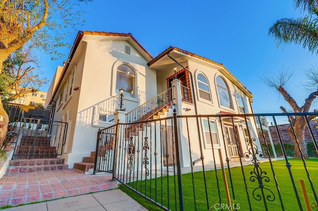 mediterranean / spanish home with stairs, a tiled roof, a front lawn, and stucco siding