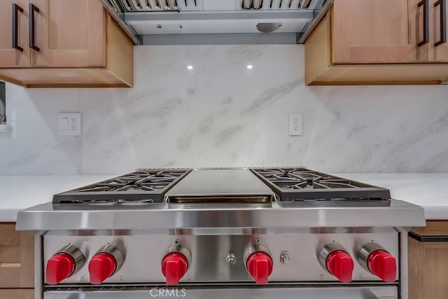 kitchen featuring backsplash, light countertops, under cabinet range hood, and high end stainless steel range