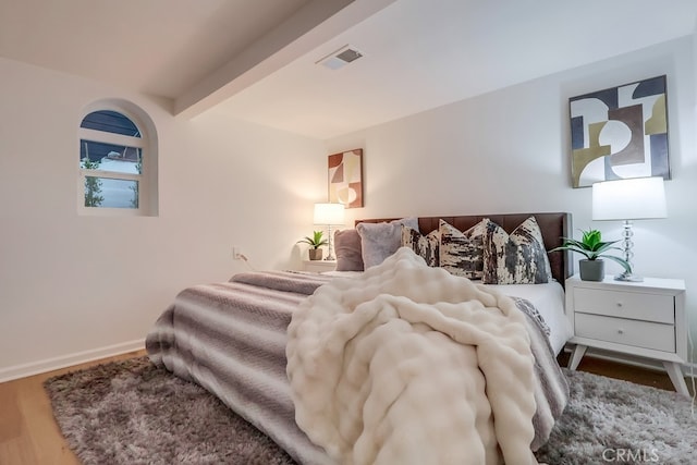 bedroom with beamed ceiling, wood finished floors, visible vents, and baseboards