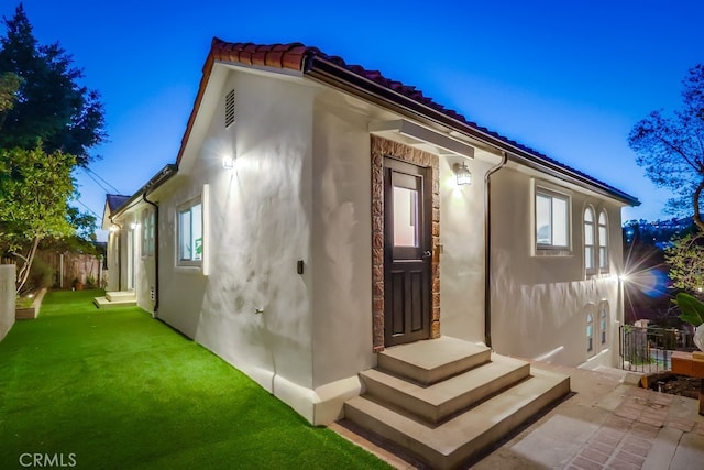 exterior space featuring fence, a yard, a tiled roof, and stucco siding