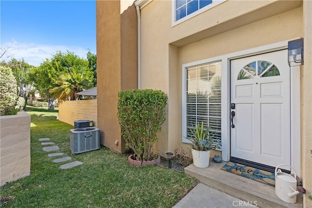 doorway to property with stucco siding, a lawn, and central air condition unit