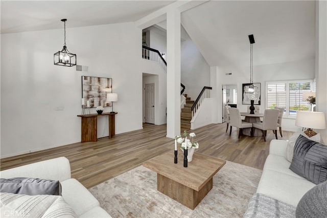 living area with visible vents, high vaulted ceiling, wood finished floors, a chandelier, and stairs