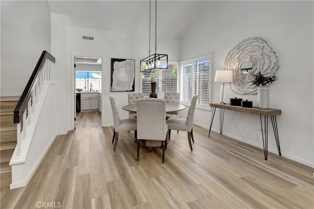 dining area featuring visible vents, stairway, a high ceiling, light wood finished floors, and baseboards