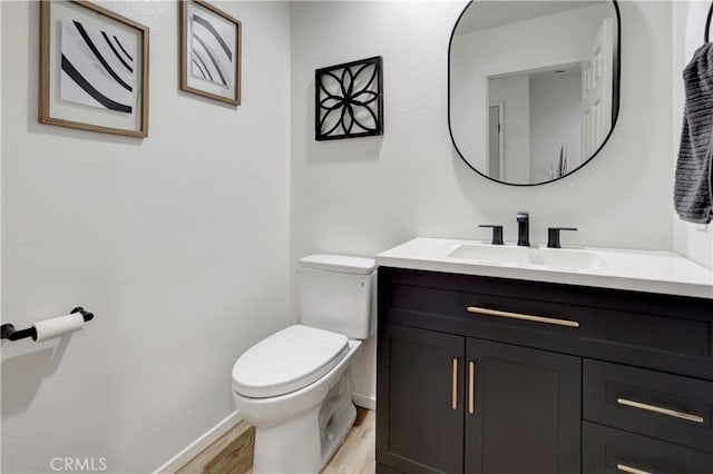 half bath with toilet, vanity, baseboards, and wood finished floors