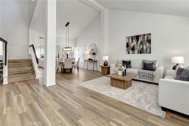 living room featuring beamed ceiling, visible vents, high vaulted ceiling, light wood-style floors, and stairs