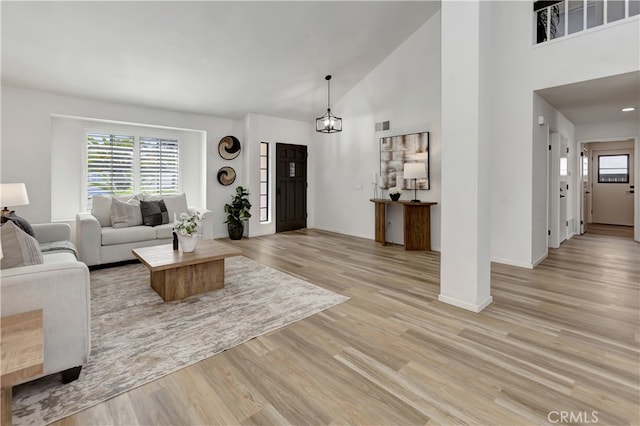 living area featuring a wealth of natural light, visible vents, light wood finished floors, and high vaulted ceiling