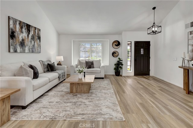 living room featuring light wood finished floors, a notable chandelier, and lofted ceiling