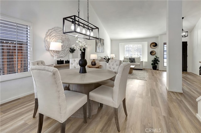 dining space featuring high vaulted ceiling, light wood-type flooring, and baseboards