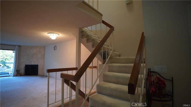 stairs with a textured ceiling, a fireplace, and carpet flooring