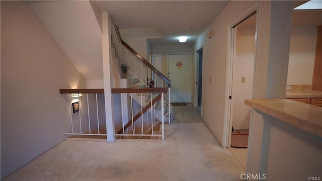 corridor with a textured ceiling, stairs, and light colored carpet