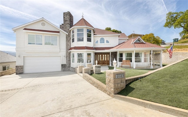 victorian home with a garage, driveway, stucco siding, a front lawn, and a chimney