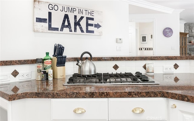 details featuring ornamental molding, backsplash, white cabinets, and stainless steel gas stovetop