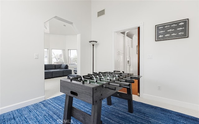 game room with carpet flooring, visible vents, a towering ceiling, and baseboards