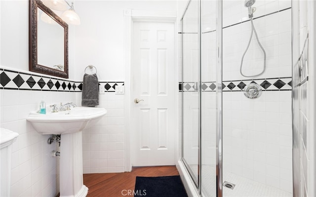 full bathroom featuring a wainscoted wall, a shower stall, tile walls, and wood finished floors