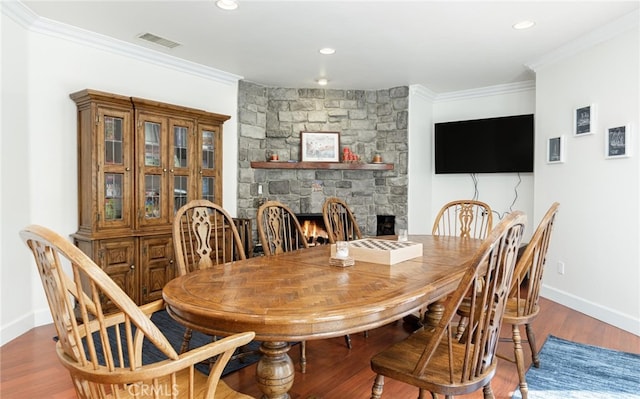 dining area featuring baseboards, visible vents, wood finished floors, crown molding, and a fireplace