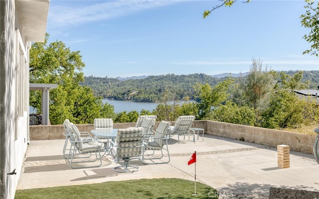 view of patio featuring a water view, a wooded view, and outdoor dining space