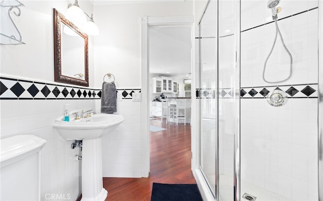 bathroom with a wainscoted wall, tile walls, toilet, a shower stall, and wood finished floors