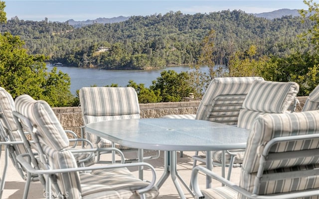 view of patio with outdoor dining space, a view of trees, and a water and mountain view