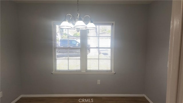 spare room with a notable chandelier, baseboards, and wood finished floors