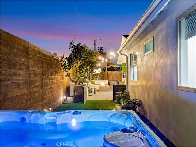 pool at dusk featuring a patio, outdoor lounge area, fence, and a hot tub