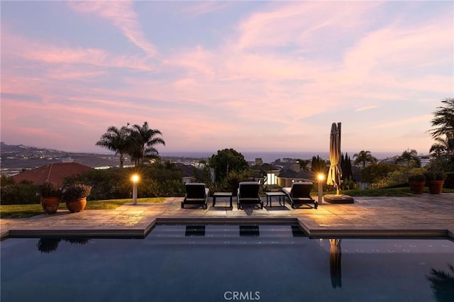 pool at dusk with an outdoor pool and a patio