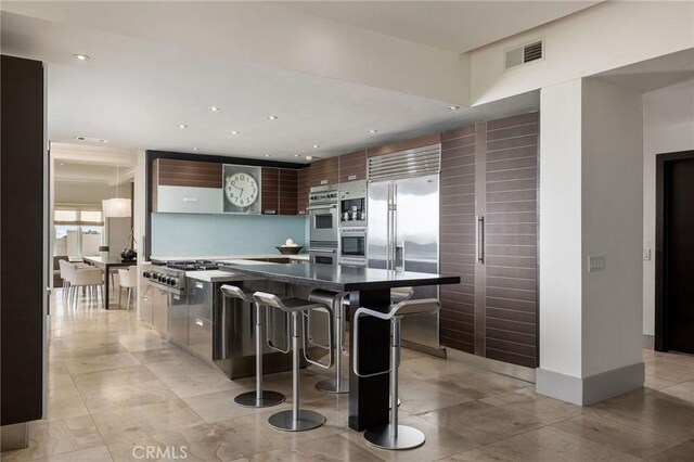 kitchen with stainless steel appliances, visible vents, a kitchen breakfast bar, backsplash, and modern cabinets