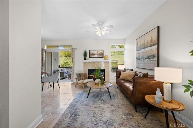 tiled living room with ceiling fan, a tiled fireplace, and baseboards