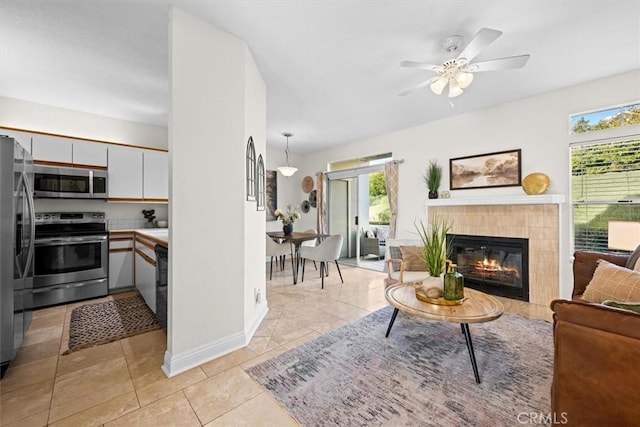 living area featuring light tile patterned floors, a tile fireplace, a ceiling fan, baseboards, and stairs