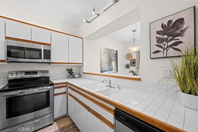 kitchen with white cabinets, tile countertops, appliances with stainless steel finishes, pendant lighting, and a sink