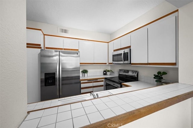 kitchen featuring appliances with stainless steel finishes, white cabinets, visible vents, and tile countertops