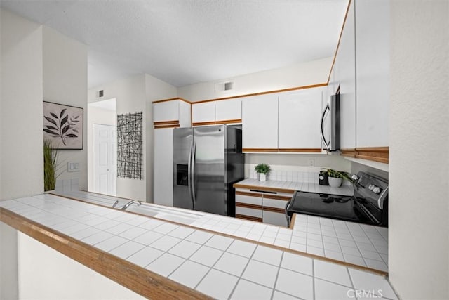 kitchen featuring stainless steel appliances, a sink, tile counters, and white cabinets