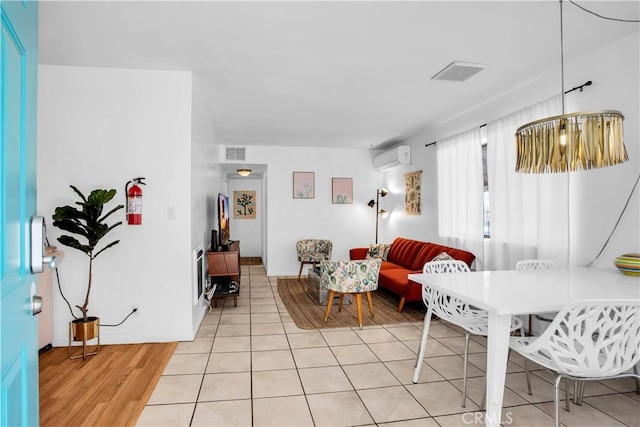 living area with a wall mounted air conditioner, visible vents, and light tile patterned floors