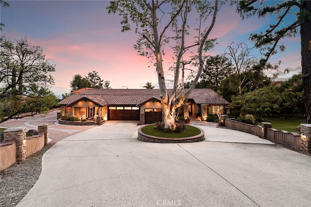 mediterranean / spanish-style home featuring concrete driveway, stone siding, a tile roof, an attached garage, and stucco siding