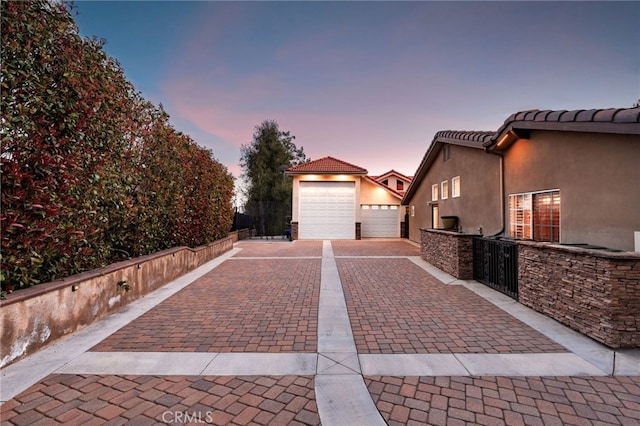 exterior space featuring a tiled roof, decorative driveway, fence, and stucco siding