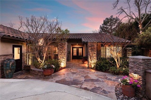 view of front of house with stone siding, french doors, a tiled roof, and stucco siding