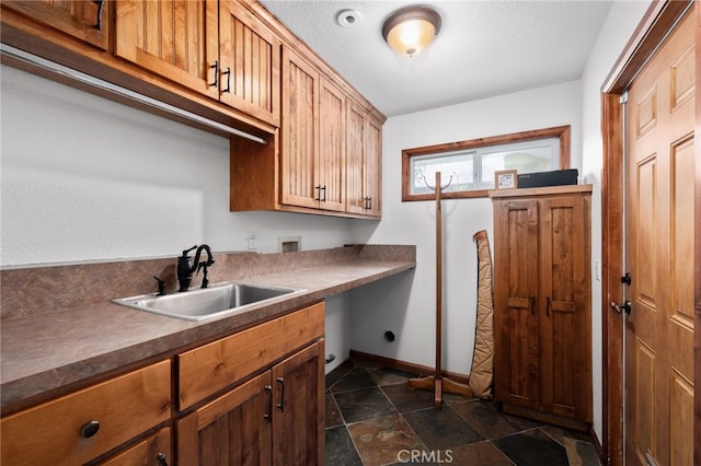 interior space featuring washer hookup, cabinet space, stone finish floor, a sink, and baseboards