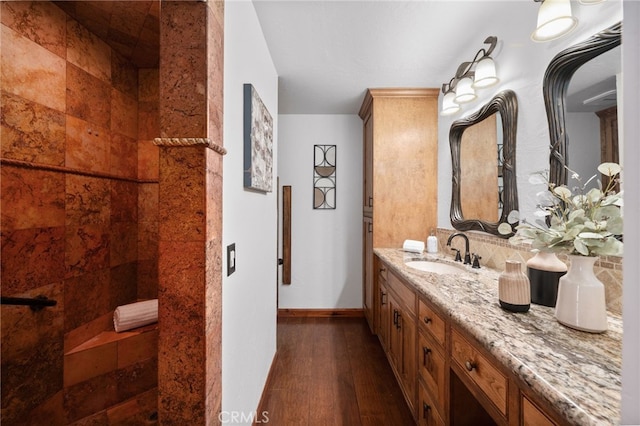 full bathroom with a tile shower, vanity, baseboards, and wood finished floors