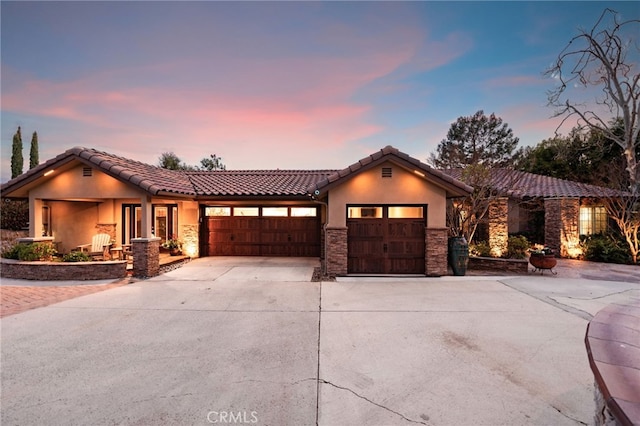 view of front facade featuring driveway, stone siding, a tiled roof, an attached garage, and stucco siding