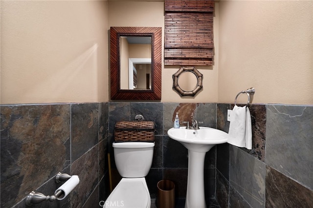 half bathroom with toilet, tile walls, and wainscoting