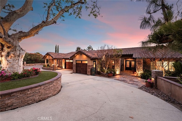 view of front of home with driveway, stone siding, a tile roof, an attached garage, and stucco siding