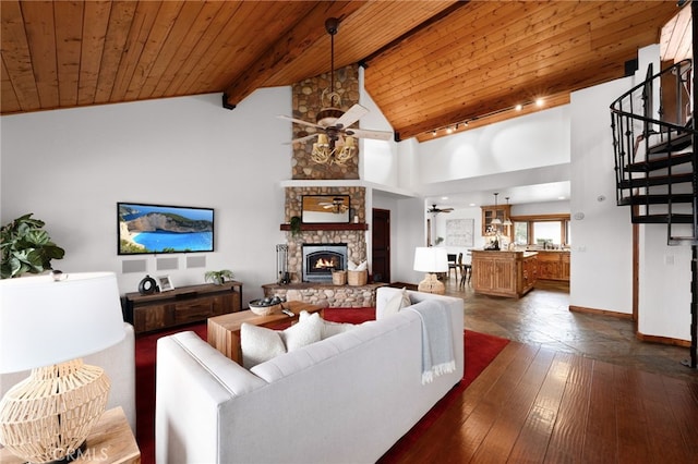 living area with wooden ceiling, ceiling fan, beamed ceiling, stairs, and a stone fireplace