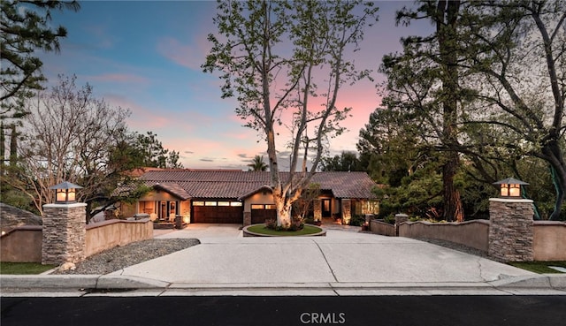 view of front of home featuring a garage, driveway, a fenced front yard, and a tile roof