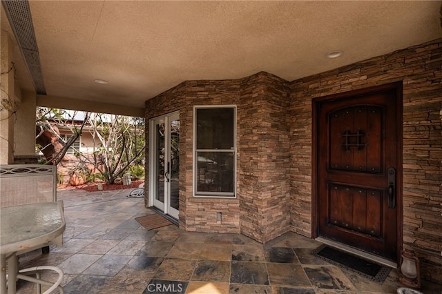 property entrance with stone siding, a patio, and french doors