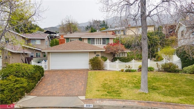 traditional-style house with an attached garage, fence, decorative driveway, a front lawn, and stucco siding