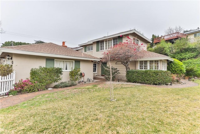 traditional-style house featuring a shingled roof, a front yard, fence, and stucco siding